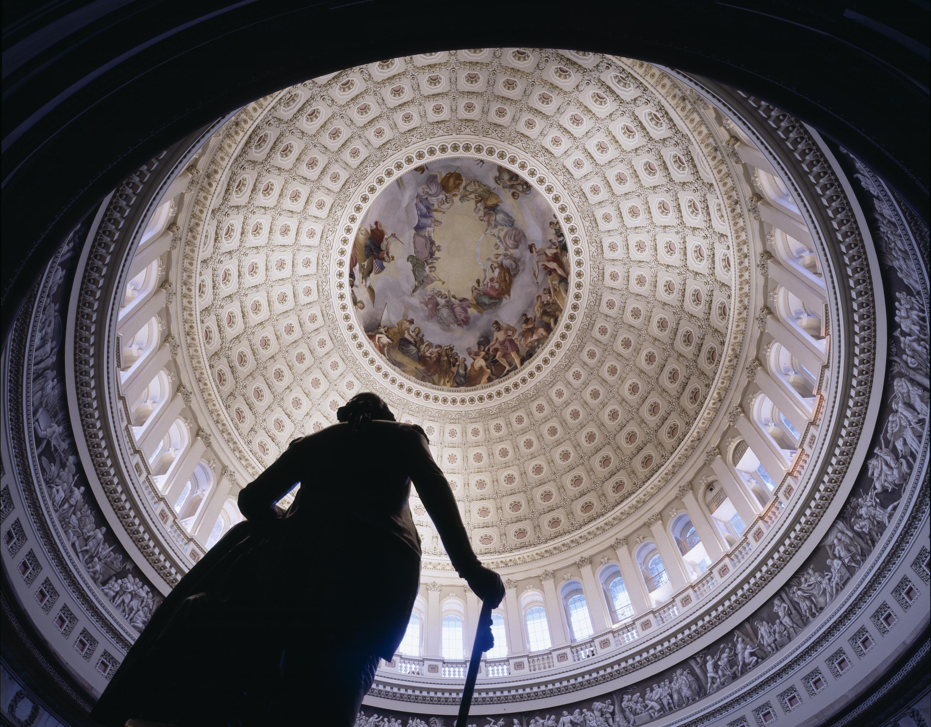 Looking straight up into the U.S. Capitol dome from beneath the rotunda, the Apotheosis of Washington fresco ringing the oculus, with the silhouette of a statue in the foreground