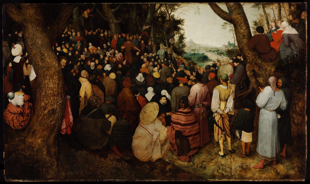 A wide painting of a crowd of several hundred people gathered in a forest clearing, most of them seen from behind, facing a small figure in a brown garment who stands far back among the trees with one arm raised. In the foreground are people in sixteenth-century Flemish dress, several in turbans and striped cloaks, and a man in a yellow-and-white slashed costume with a sword at his side. On the right, beyond the trees, a river winds through a valley toward a distant town.