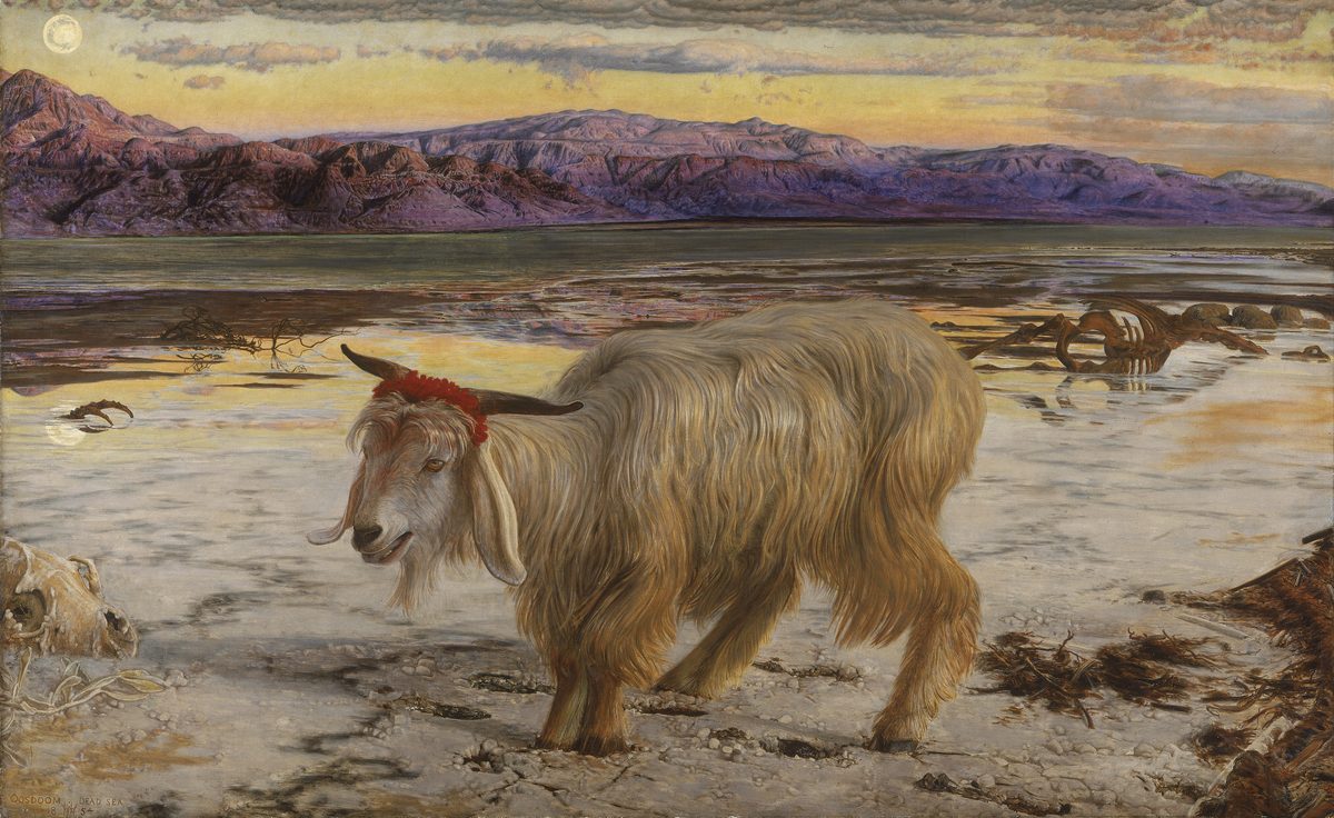 A solitary white and tan goat stands on the salt-crusted, bone-littered shore of the Dead Sea at sunset, a band of scarlet wool tied around its horns. Skeletal remains lie half-buried in the salt around its feet. Behind it, the flat, discolored water stretches to a ring of bare purple mountains under a streaked orange and grey sky.