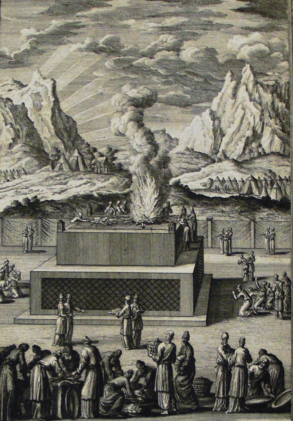 A wide baroque scene at the bronze altar: smoke and fire rise from a heap of wood and pieces on top of a large stepped platform, a robed and turbaned priest standing beside the fire. On the ground below, clustered groups of worshippers in flowing robes bring animals and look on, with the tents of the wilderness camp and two tall mountain peaks filling the background.