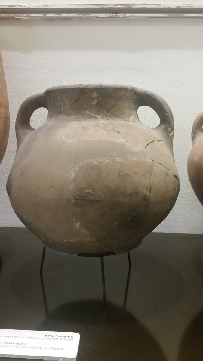 A two-handled ceramic cooking pot, cracked and repaired, excavated and displayed on a metal stand in a museum case, with a label reading 'cooking pot, Tel Amal, Late Israelite (Iron) Period'.
