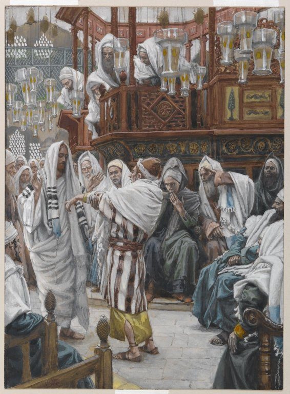 A gouache painting of a synagogue interior, hung with rows of glass oil lamps and dominated by an elevated wooden reading platform crowded with turbaned onlookers. In the foreground Jesus, in white, stands at left with his hand raised; a man in a striped robe steps toward him holding out his arm, while seated men in prayer shawls watch with folded arms and skeptical faces.
