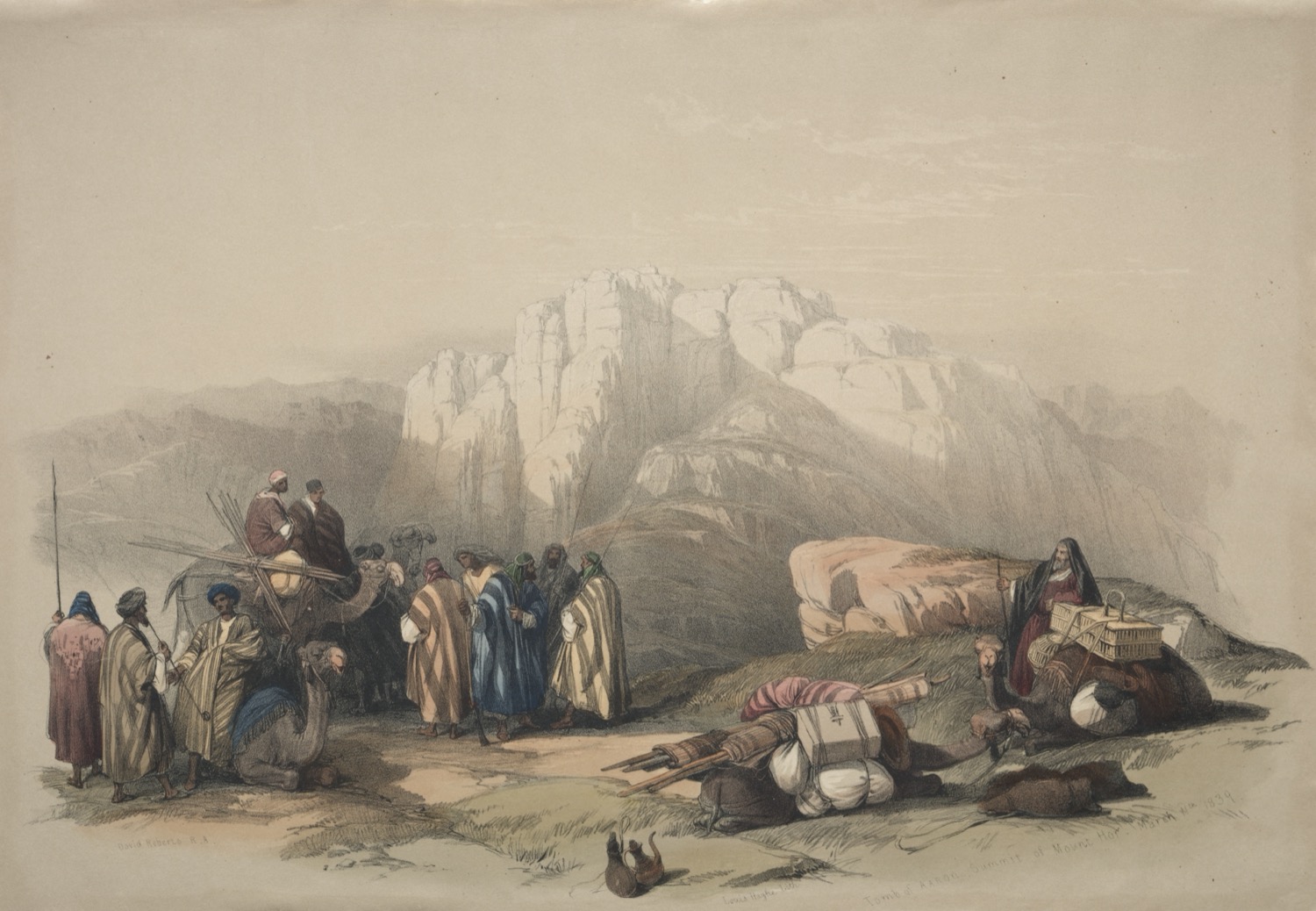 A hand-coloured lithograph. A caravan has halted on stony ground in the foreground: robed men in striped and blue cloaks stand talking, camels kneel among bundles and tent-poles, and at the right a bearded man in a dark red robe leans on a staff beside a loaded animal. Behind them the ground rises through brown foothills to a pale, near-white massif of banded rock with a flat-topped, cliff-walled summit, hazy against a blank sky.