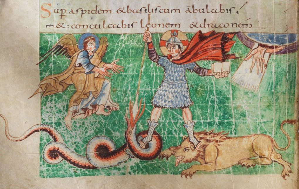 A manuscript page. Across the top, two lines of Latin in red and brown ink. Below, on a green cross-hatched ground, a haloed figure in a mail shirt and helmet with a red cloak stands with legs apart, gripping a long spear. His left foot presses down the head of a long red-and-white banded serpent whose coils fill the lower left and whose tail runs off the edge of the picture; his right foot presses down the head of a snarling tawny lion lying at the lower right. A winged angel leans in from the left with both hands open toward him, and a hand reaches down out of drapery at the upper right.