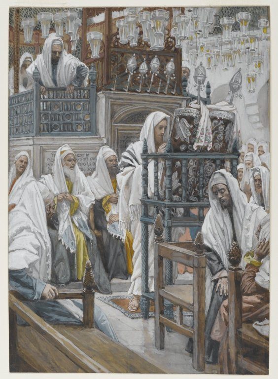 A painting of the inside of a synagogue crowded with men wrapped in white prayer shawls. In the centre Jesus, in a white shawl with dark stripes, stands at a tall carved wooden reading desk on which a scroll rests in a decorated case. Older men sit on benches to the left, others crowd in at the right, a man leans over the rail of a gallery above, and dozens of glass oil lamps hang from the ceiling.