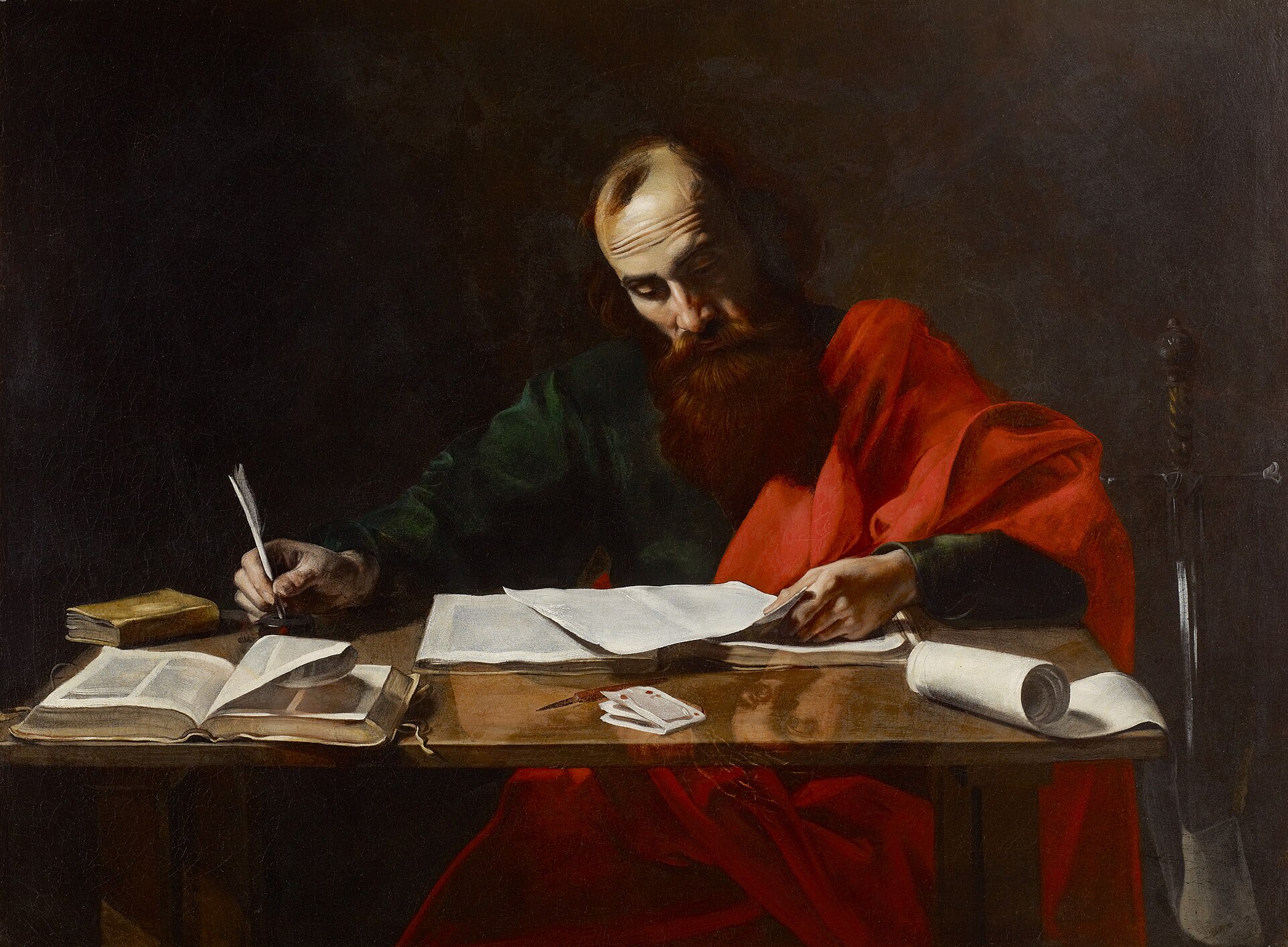 A balding, red-bearded man in a green tunic and red cloak bends over a table in near-darkness, a quill in one hand and loose sheets under the other, with open books, a rolled scroll and the hilt of a sword beside him