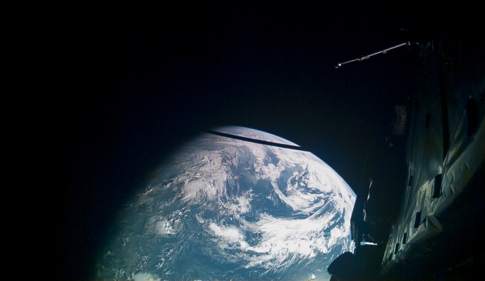 Earth's blue, cloud-swirled limb glowing against black space, photographed from JUICE's own cameras with the spacecraft's magnetometer boom and folded solar-array panels visible in the foreground