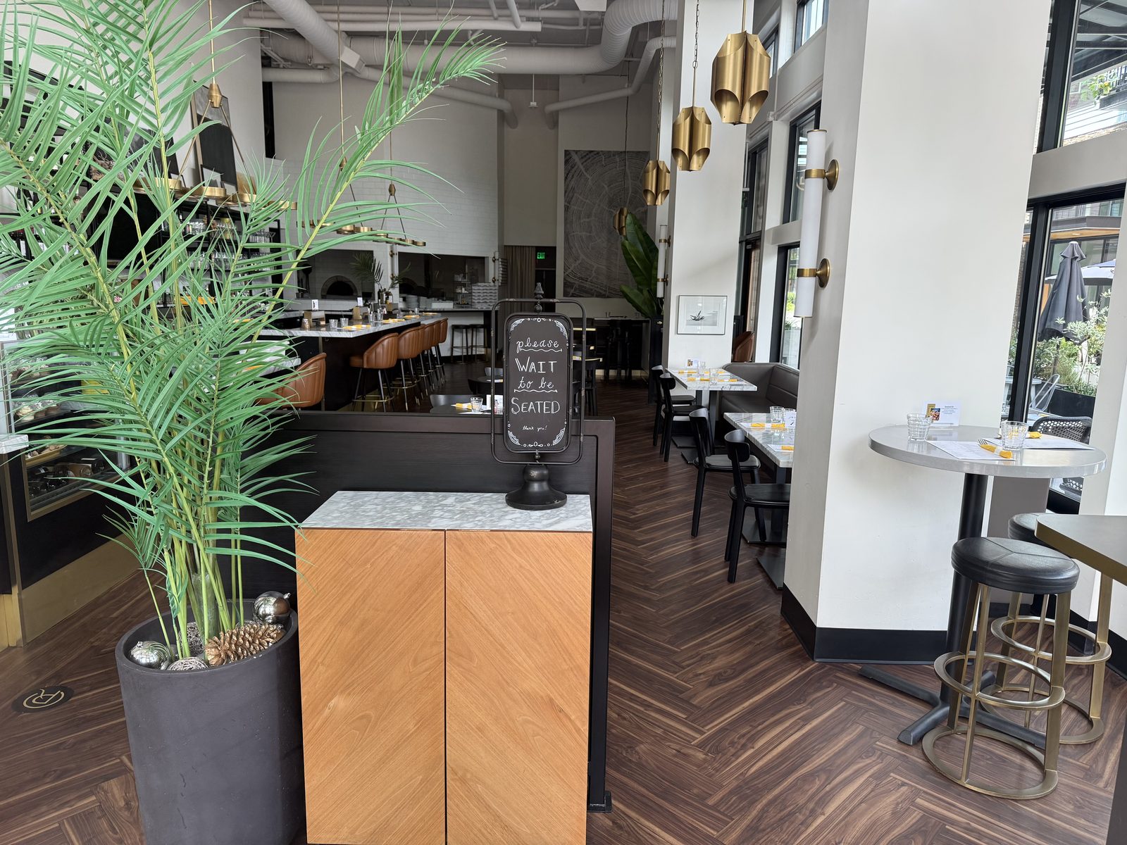 The dark wood, herringbone-floor dining room at Chuckie Pies, empty tables set for dinner, a please-wait-to-be-seated sign on the host stand