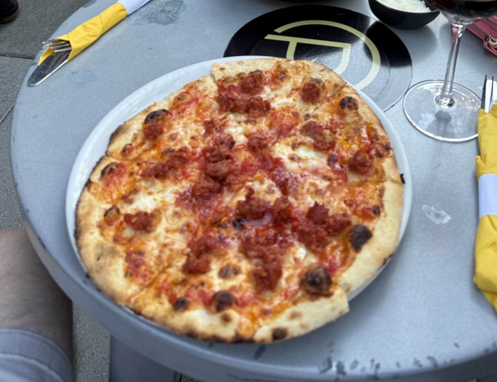 A ten-inch Neapolitan sausage pizza on a white plate at Chuckie Pies, tomato sauce and melted mozzarella scattered with irregular crumbles of fennel sausage, the puffed pale rim blistered with dark charred spots