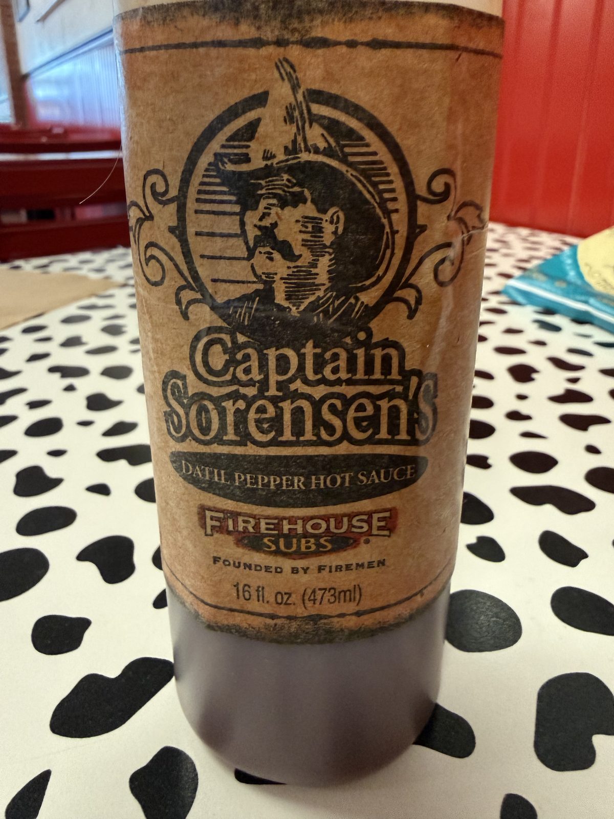 A close-up of a bottle of Captain Sorensen's Datil Pepper Hot Sauce, labeled Firehouse Subs, Founded by Firemen, 16 fl. oz.
