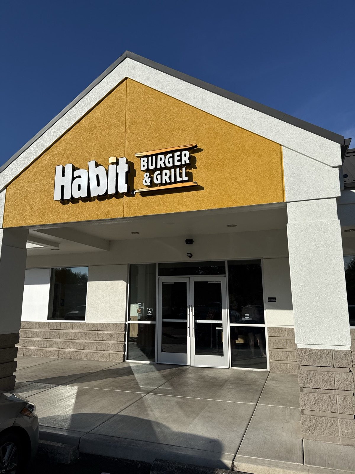 The yellow gable and white lettering of the Habit Burger & Grill sign above the entrance in Vancouver, Washington, photographed from the parking lot under a clear evening sky
