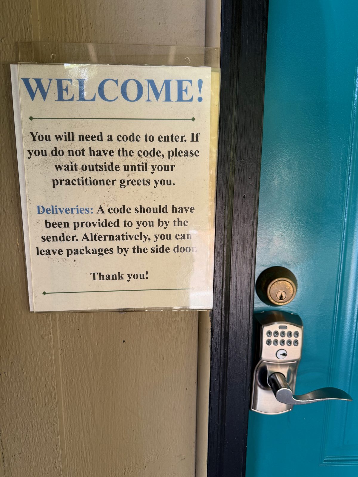 A laminated WELCOME sign taped beside a teal door with a keypad lock, explaining that a code is required to enter and that visitors without one should wait outside for their practitioner
