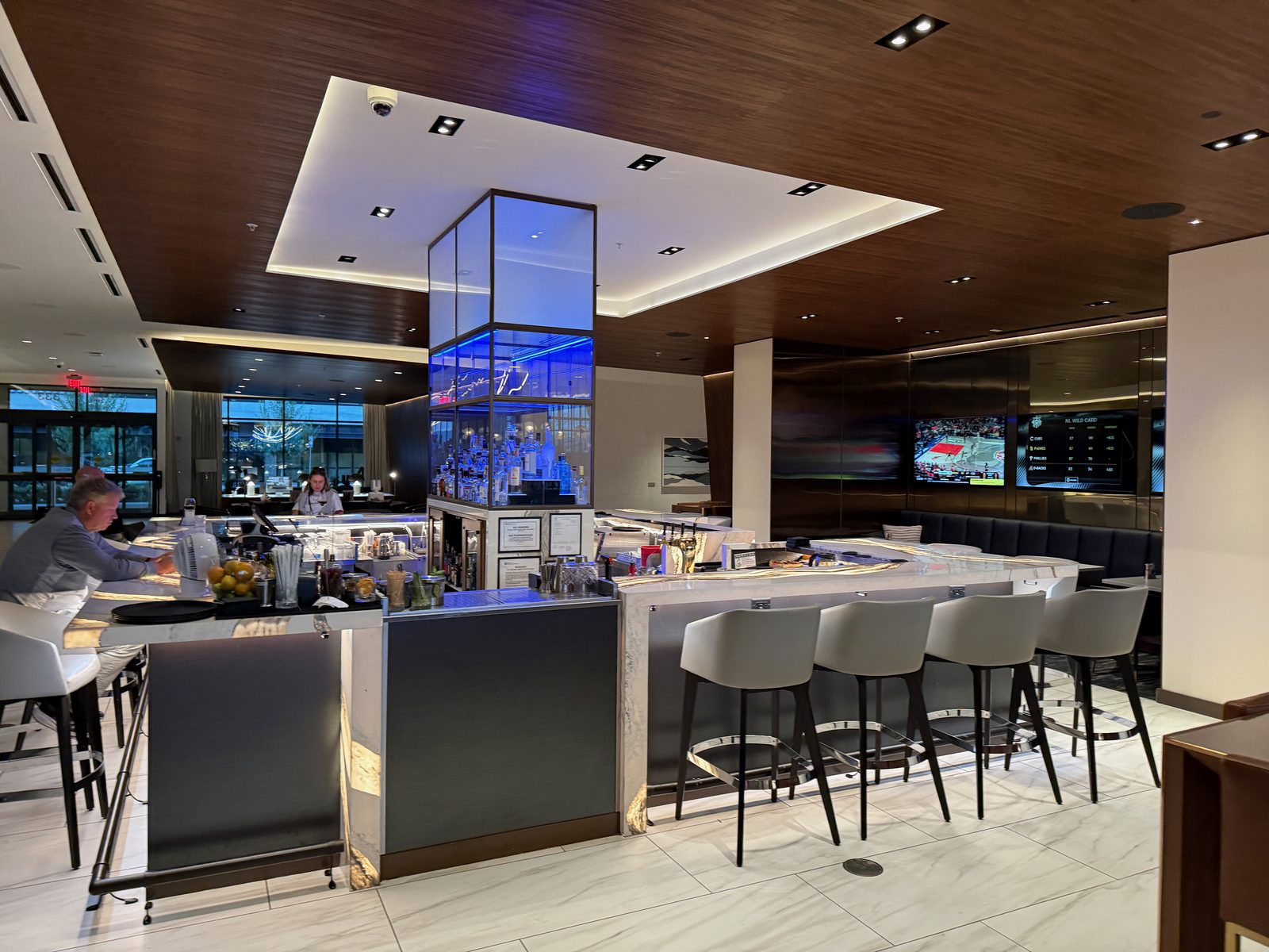 The centerpiece bar at Ondus on the Waterfront, a blue-lit glass liquor display tower rising through the ceiling, with bartenders working and patrons seated at the bar