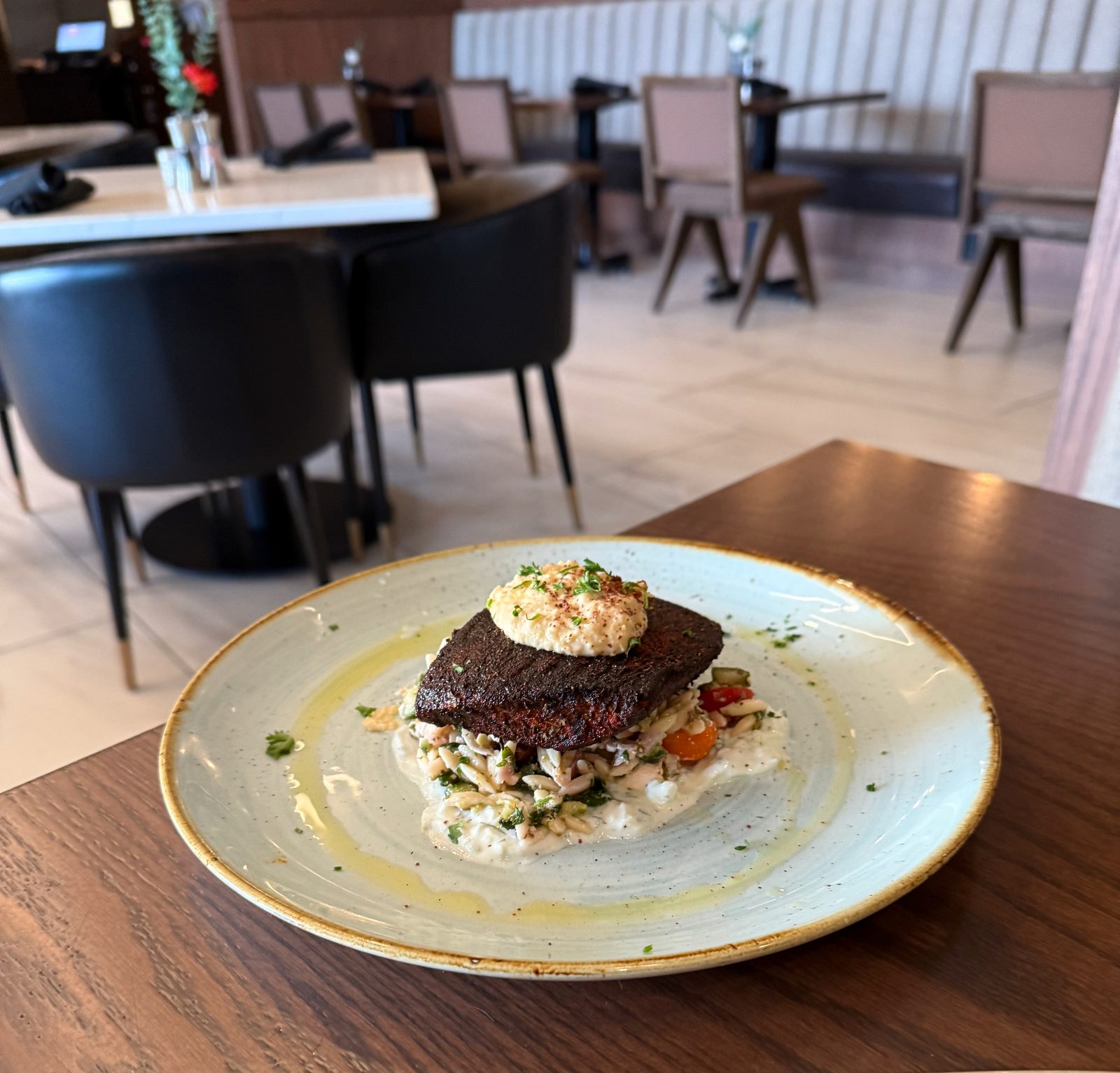 The Mediterranean Salmon plated on a table at Ondus on the Waterfront, dining room and diners visible behind it in the evening light