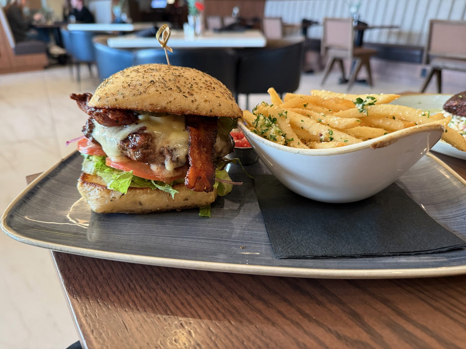 The Waterfront Burger at Ondus, a bacon cheeseburger with lettuce and tomato on a seeded bun, sliced in half, served with a bowl of truffle-parmesan fries