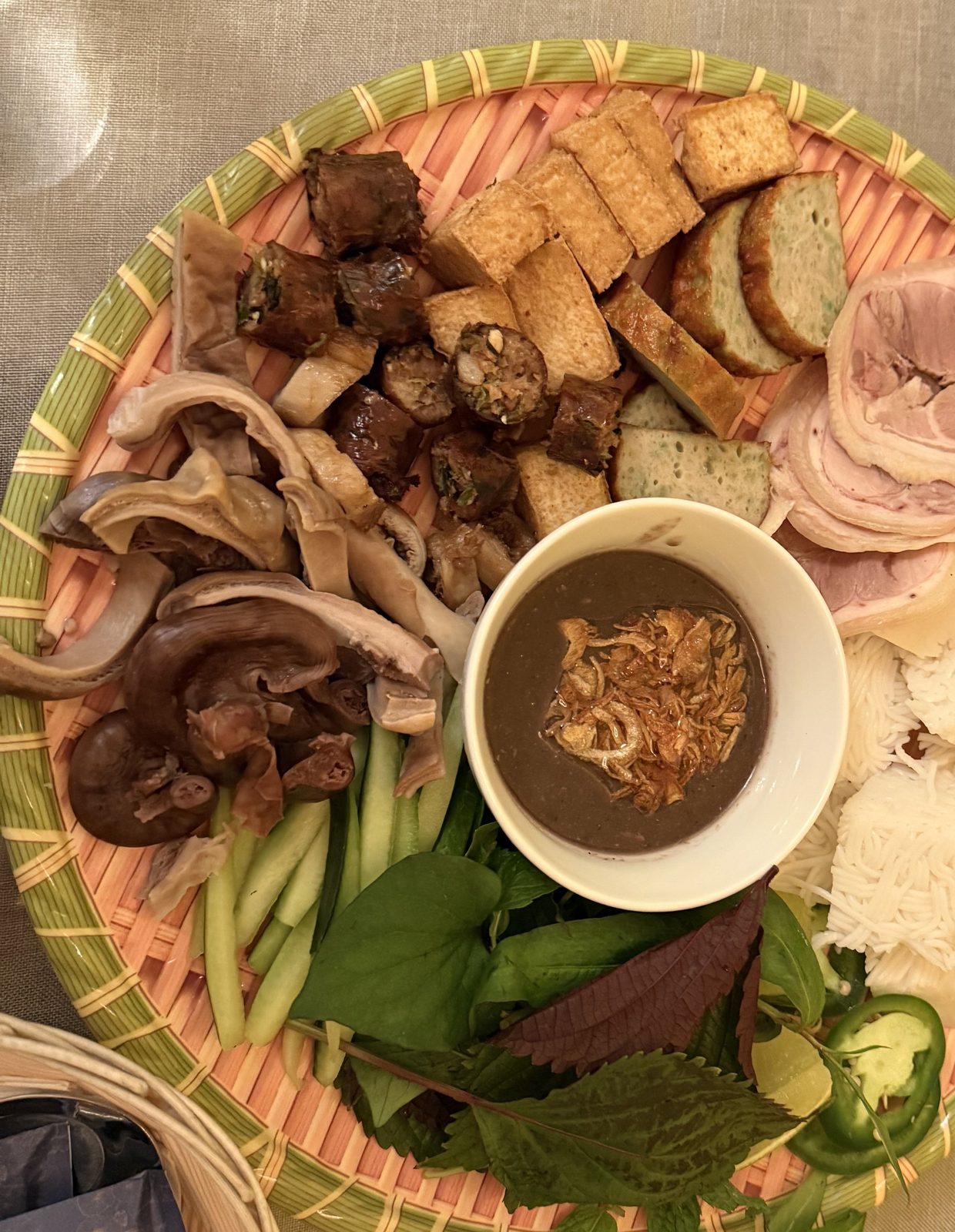 A Vietnamese platter at Pho Hathanh — fried tofu, sliced cold cuts, wood ear mushrooms, a rice noodle cake, cucumber, and fresh herbs arranged around a small bowl of dark dipping sauce topped with fried shallots