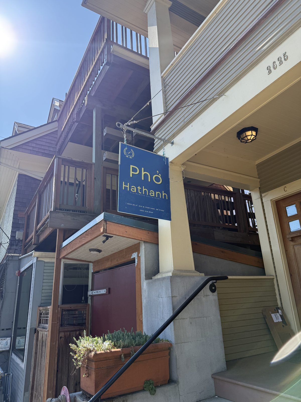 A blue hanging sign reading Pho Hathanh, Vietnamese Restaurant, with the address 2625 SE 21st Ave B, Portland, OR 97202 and a phone number, mounted on a porch post