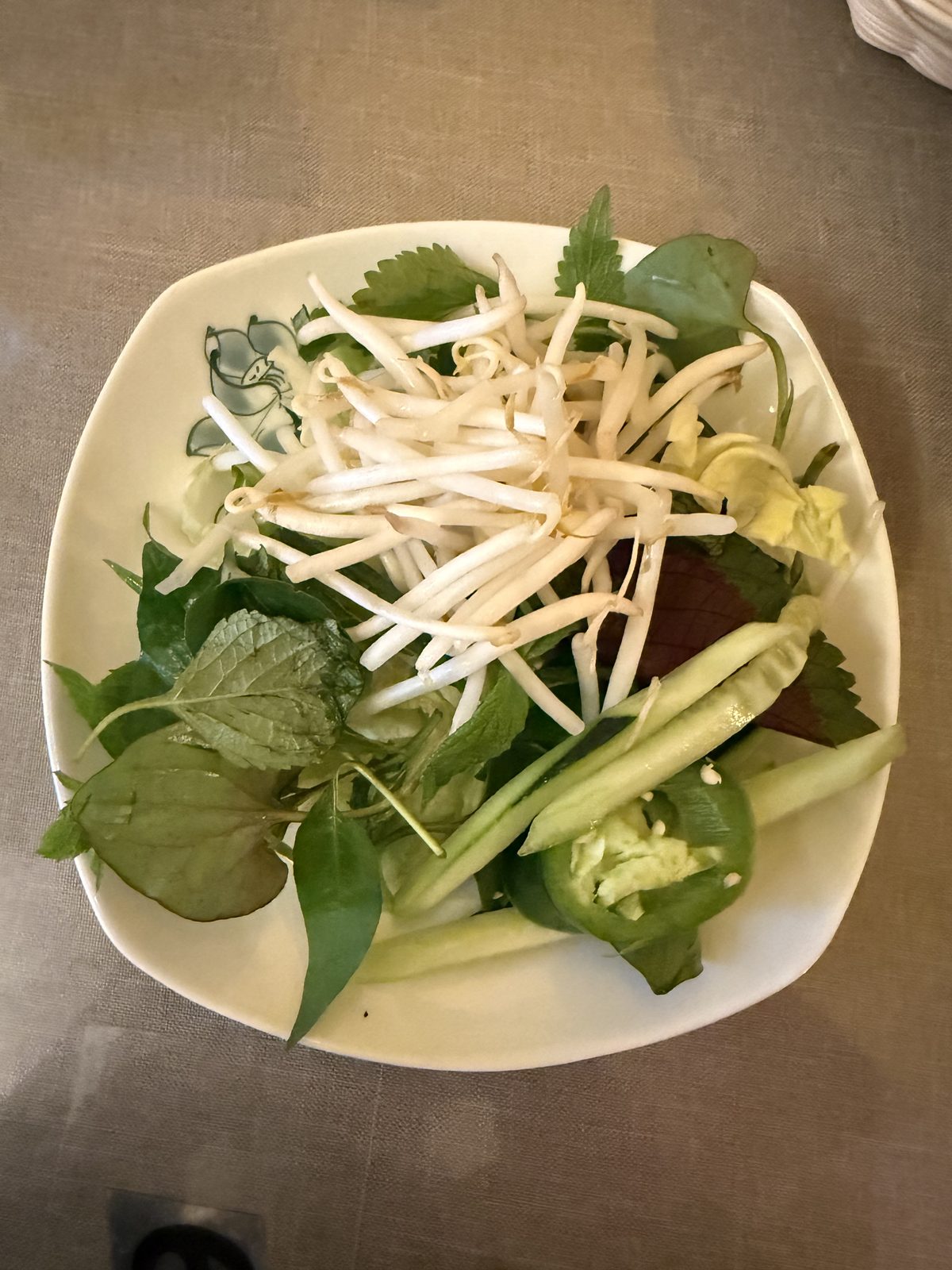 A plate of fresh herbs for bún chả at Pho Hathanh — bean sprouts, Thai basil, perilla, cucumber spears, and sliced jalapeño