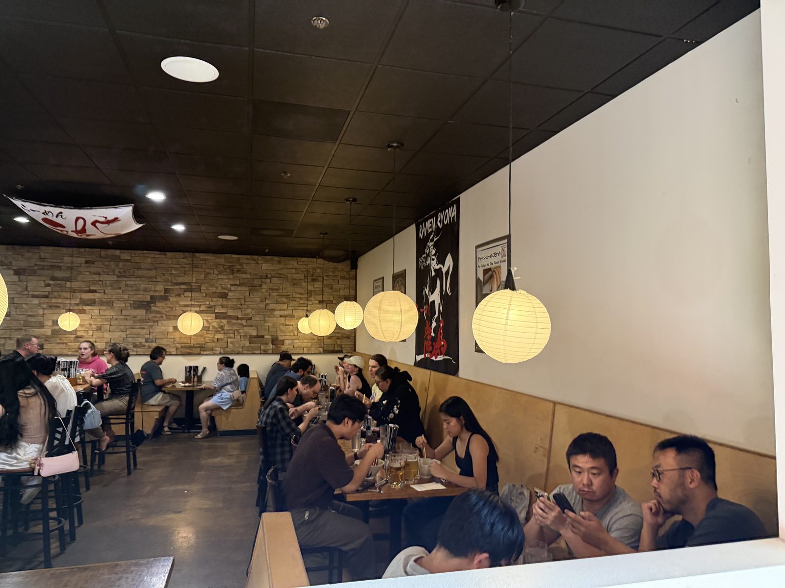 A full dining room — paper lanterns hanging over booths and a stone-veneer wall, every table occupied