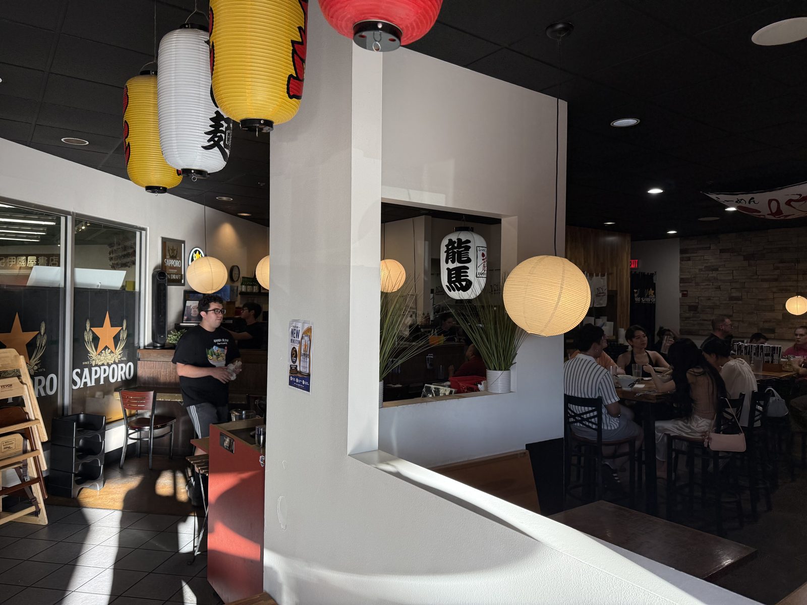 Interior — a black 龍馬 lantern and round paper lanterns over the room, a Sapporo sign, and the Kinokuniya bookstore visible through the front window