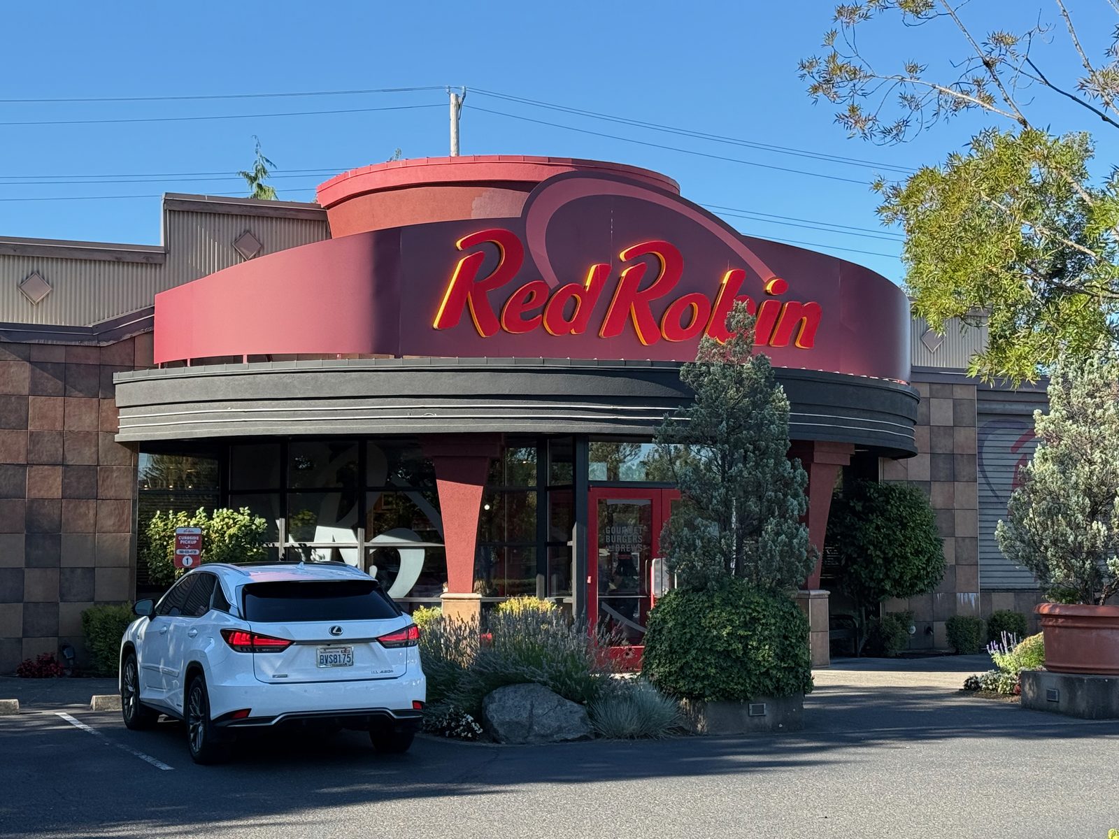 The Red Robin on SE 160th Avenue in Vancouver, Washington, photographed from the parking lot on a clear evening — a low brick building with a round red rotunda over the entrance and the Red Robin script in red neon lettering across it, against a cloudless blue sky