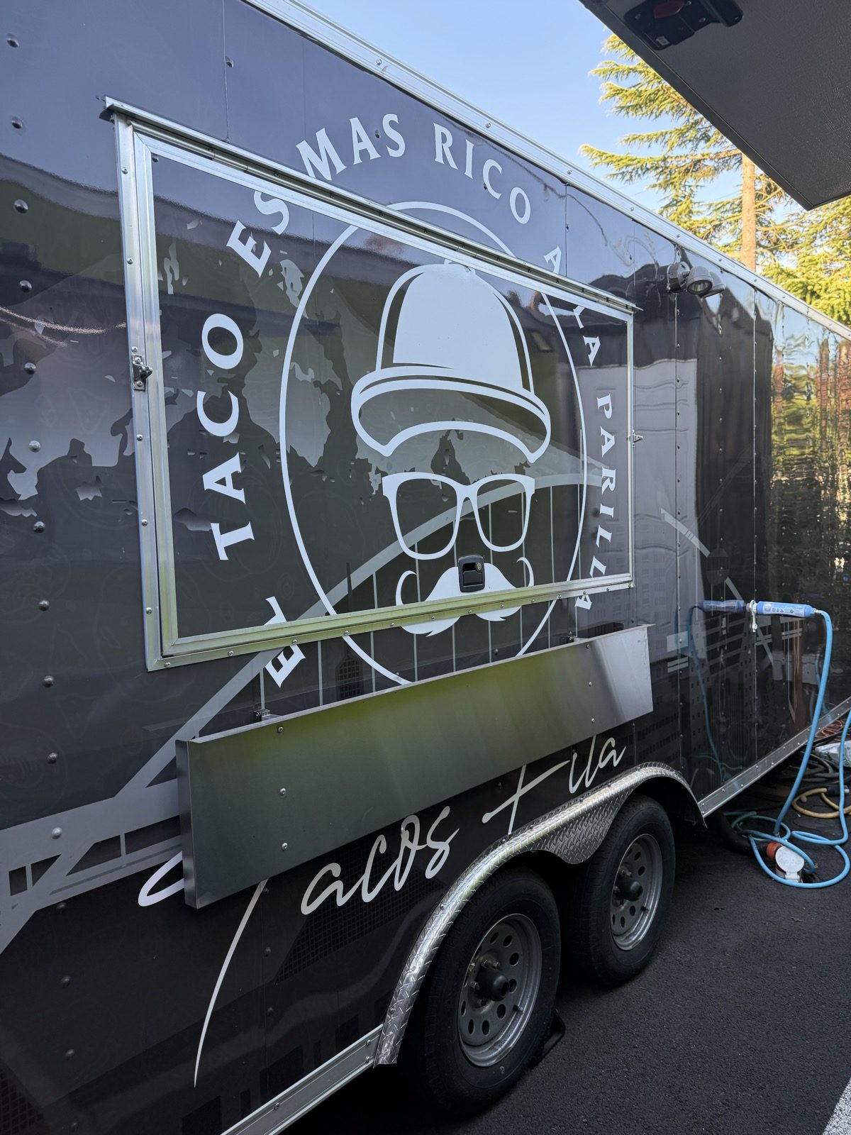 Close-up of the Tacos Fita logo on the side of the food truck — a mustached man in a wide-brimmed hat and sunglasses inside a circle, with the slogan El Taco Es Mas Rico A La Parilla, the taco is tastier grilled