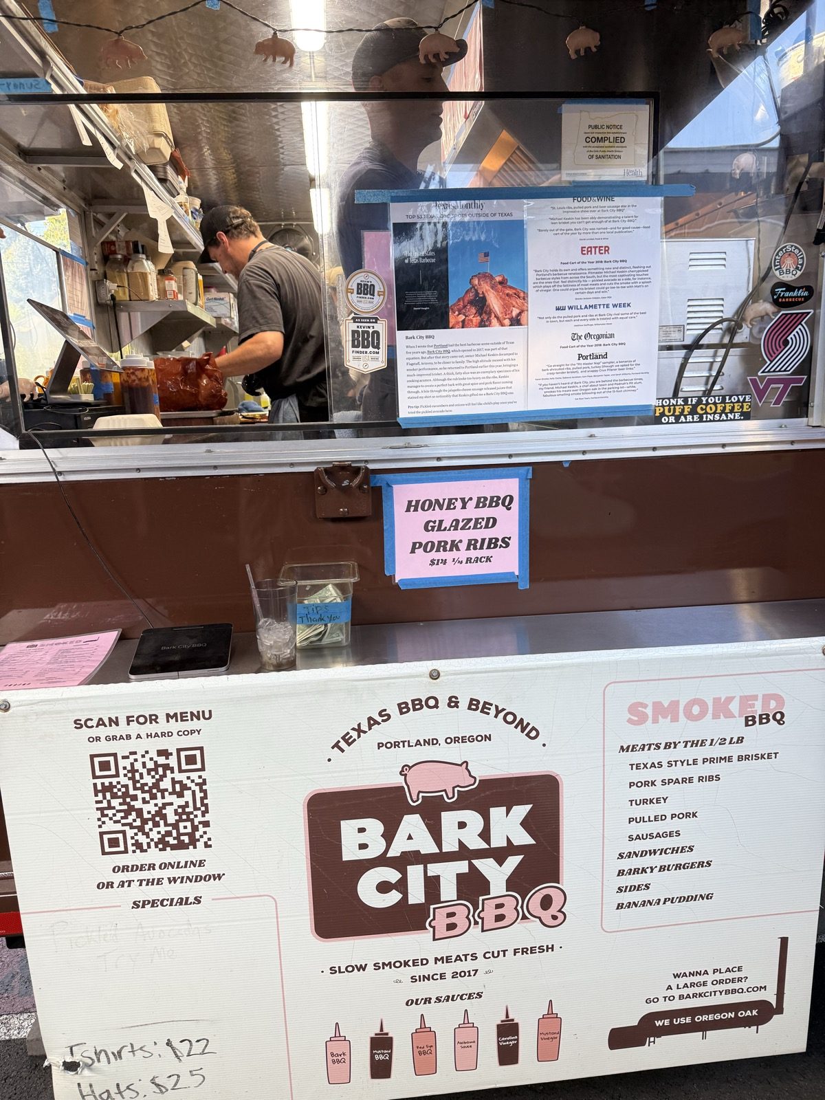 The Bark City BBQ menu board at The Heist, reading Texas BBQ & Beyond, Smoked BBQ meats by the half pound including Texas style prime brisket, pork spare ribs, turkey, pulled pork and sausages, plus sandwiches, sides and banana pudding, with a QR code to order online