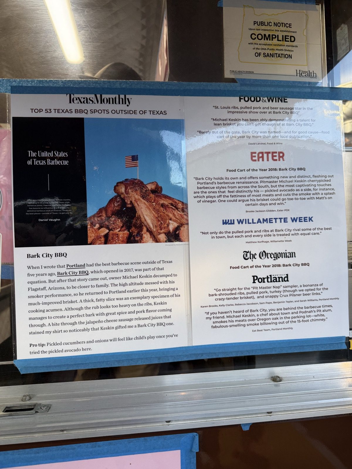 A page of press clippings taped in the order window at Bark City BBQ, including Texas Monthly's Top 53 Texas Barbecue Spots Outside of Texas, Food & Wine, Eater and The Oregonian both naming it Portland's 2018 Food Cart of the Year, Willamette Week and Portland Monthly
