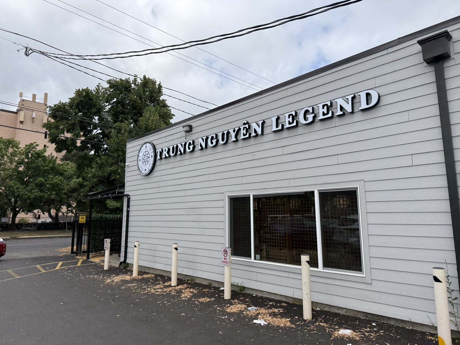 The charcoal-gray exterior of Trung Nguyên Legend on SE Powell Boulevard, a round compass-style emblem beside large black block letters reading TRUNG NGUYÊN LEGEND along the roofline