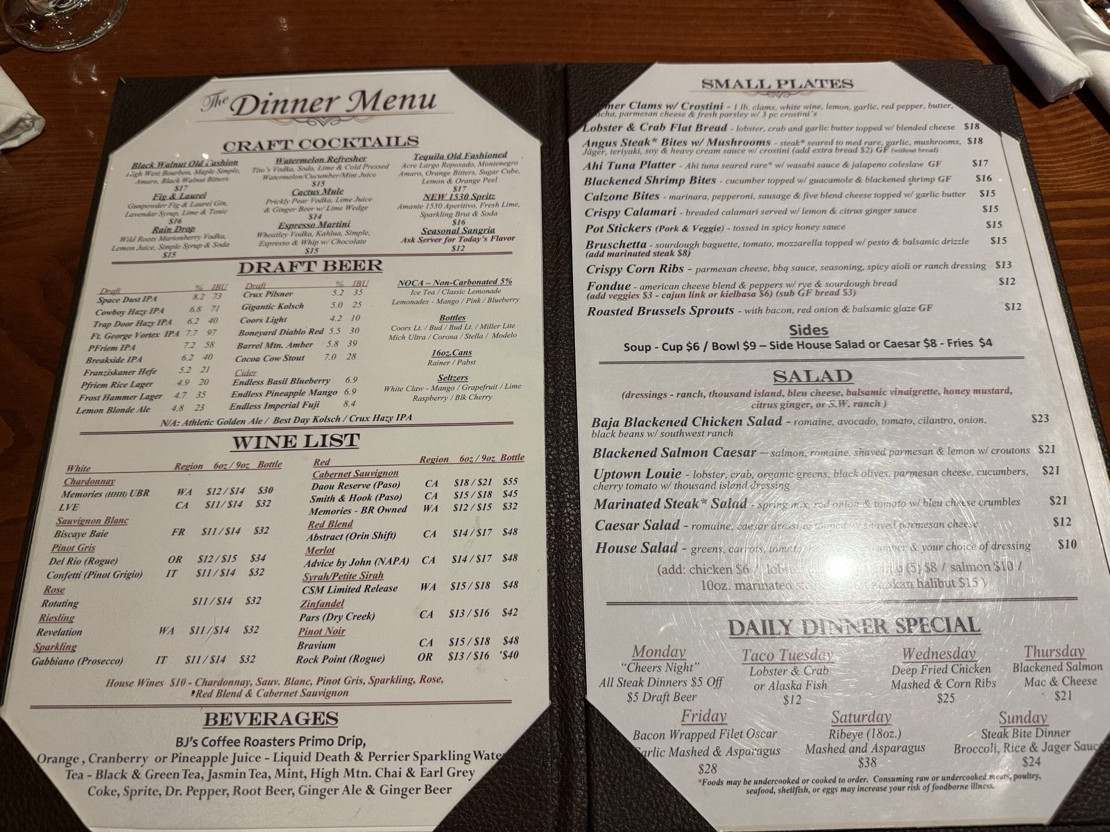 The dinner menu page showing craft cocktails, a long list of draft beers with ABV and IBU figures, a wine list by glass and bottle, and a facing page of small plates, salads and the daily dinner specials for each night of the week